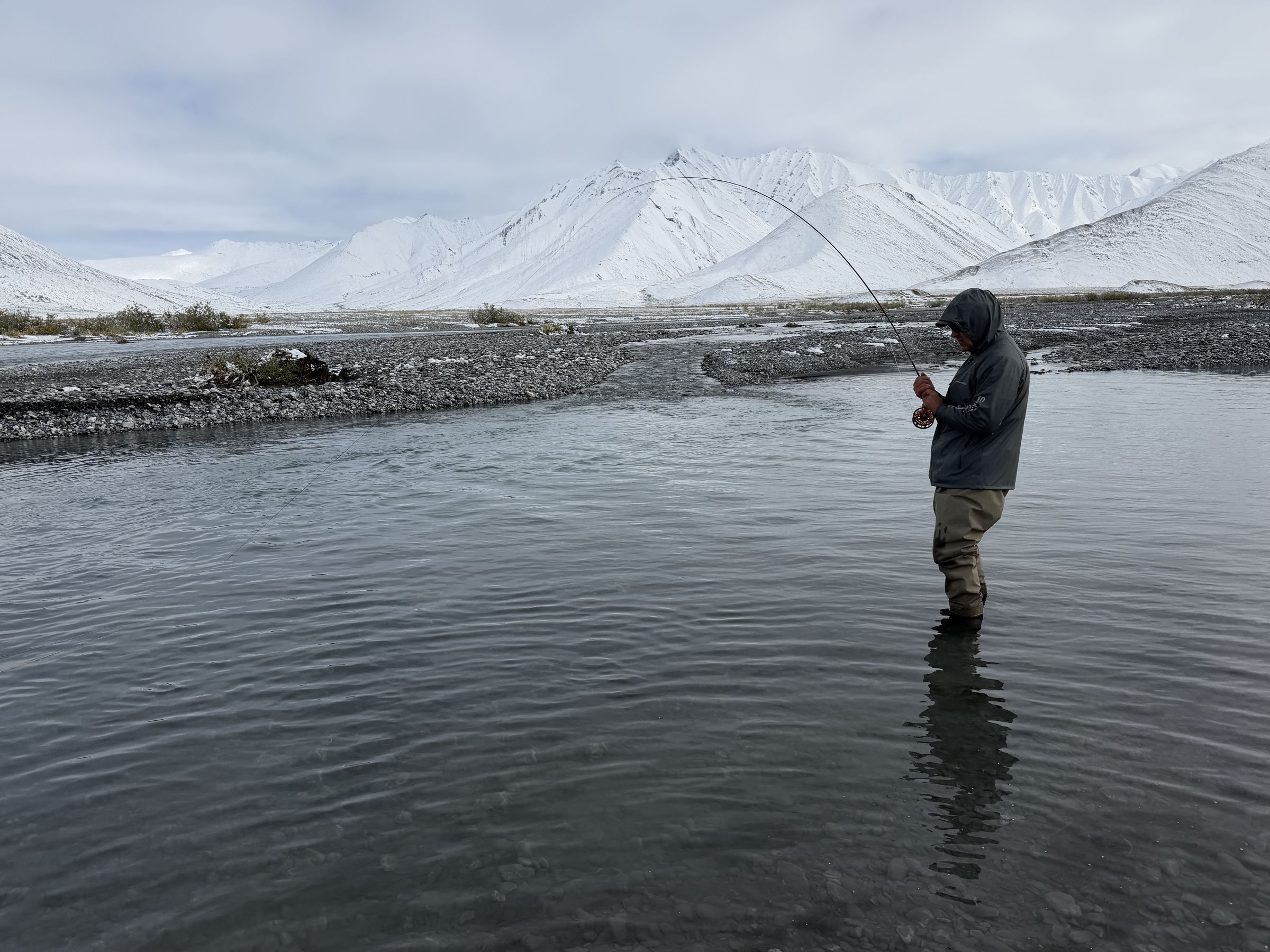 An angler fishes the Ivishak River in front of snow-dusted Brooks Range peaks.